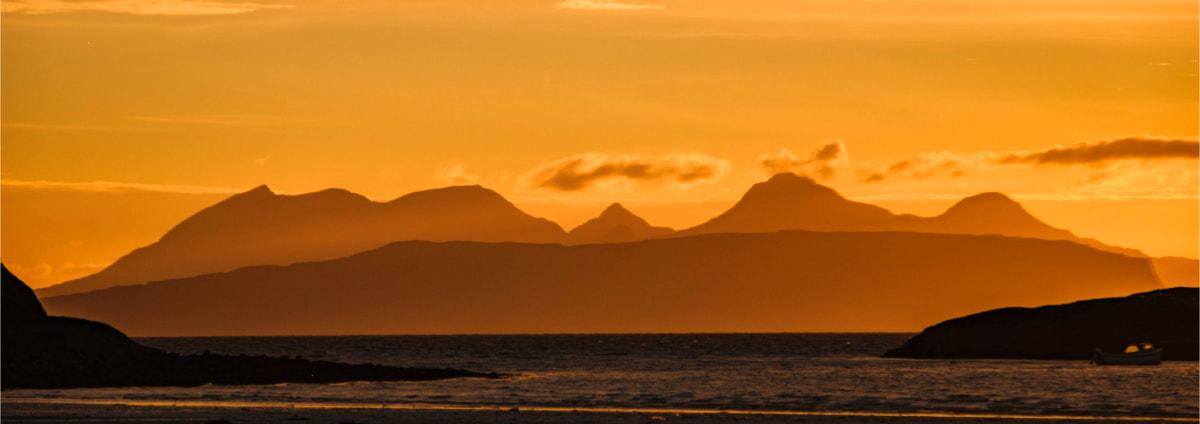 The Small Isles of Eigg and Rùm silhouetted against an orange sunset sky. Samalaman Bay, Glenuig | Moidart, Scotland | Steven Marshall Photography